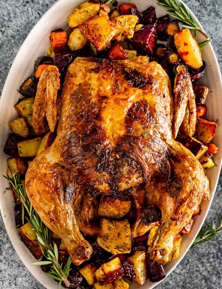 a roasted chicken on a serving platter along some roasted root veggies.