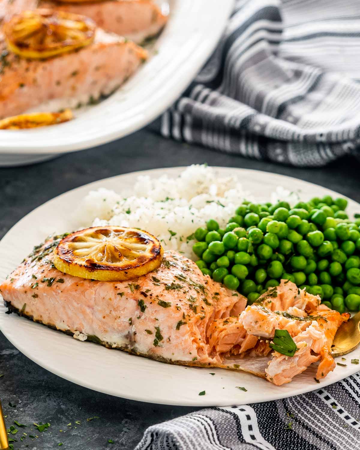 a baked salmon fillet on a white plate with peas and rice.