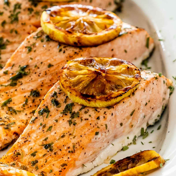 baked salmon with lemon slices on a white platter.