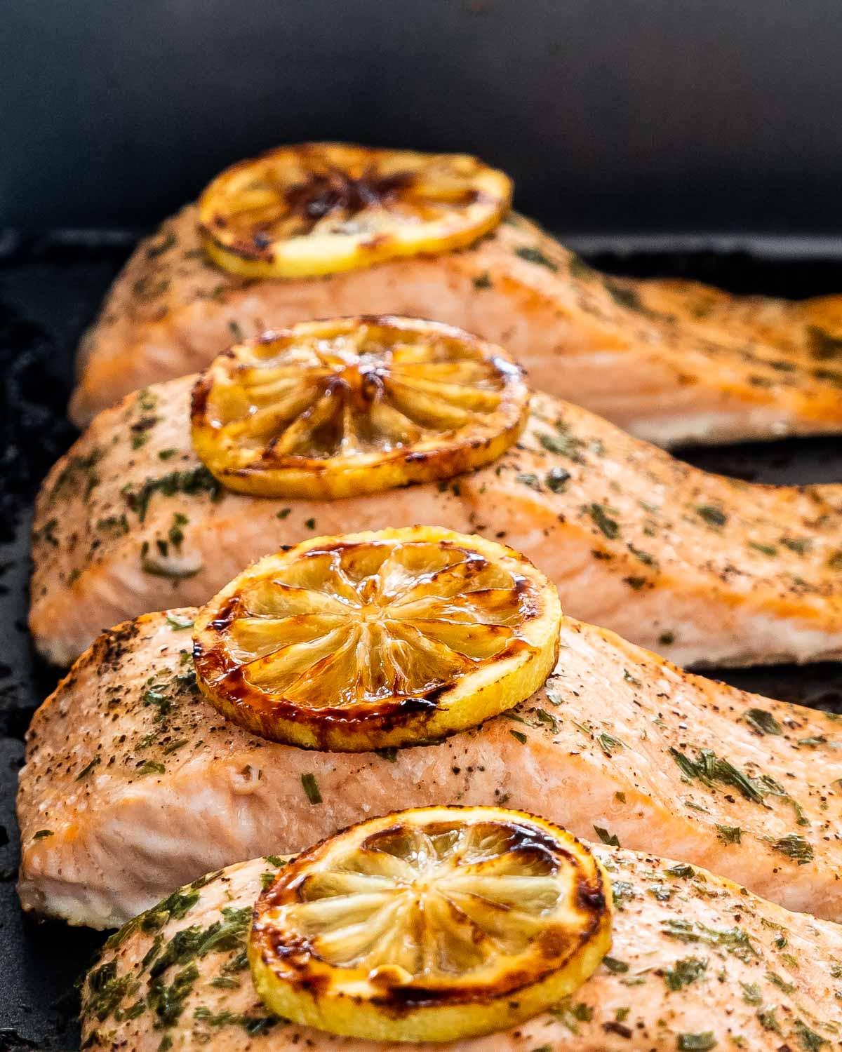 baked salmon fillets with a lemon slice on each fillet in a baking dish.