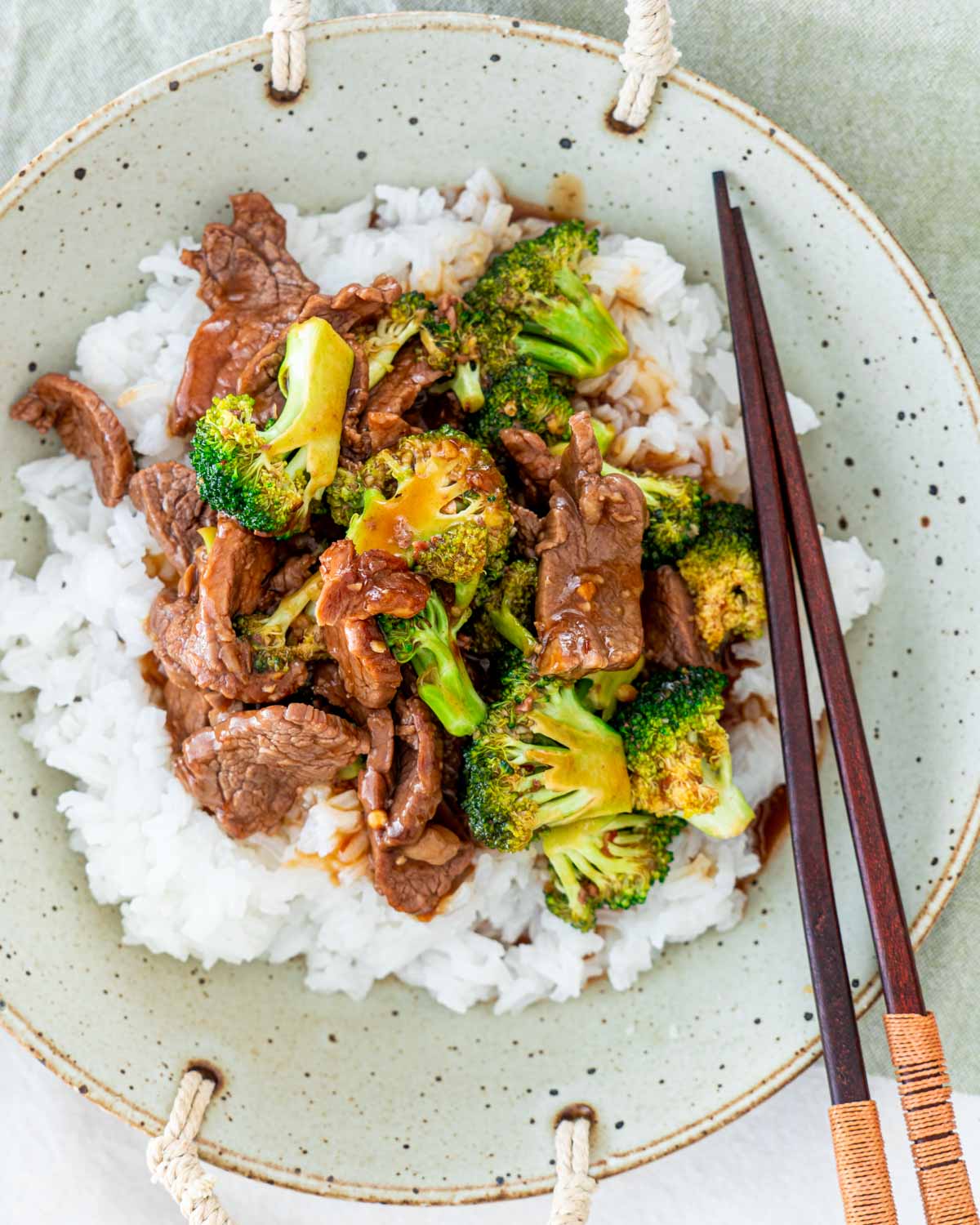 overhead shot of beef and broccoli over a bed of rice in a plate with chopsticks
