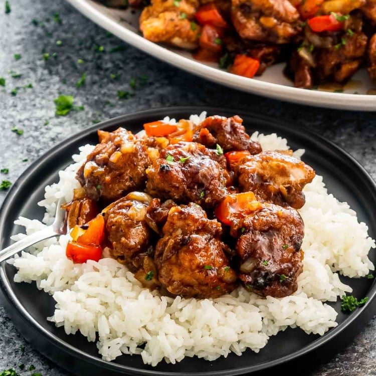 black pepper chicken on a bed of rice on a black plate.