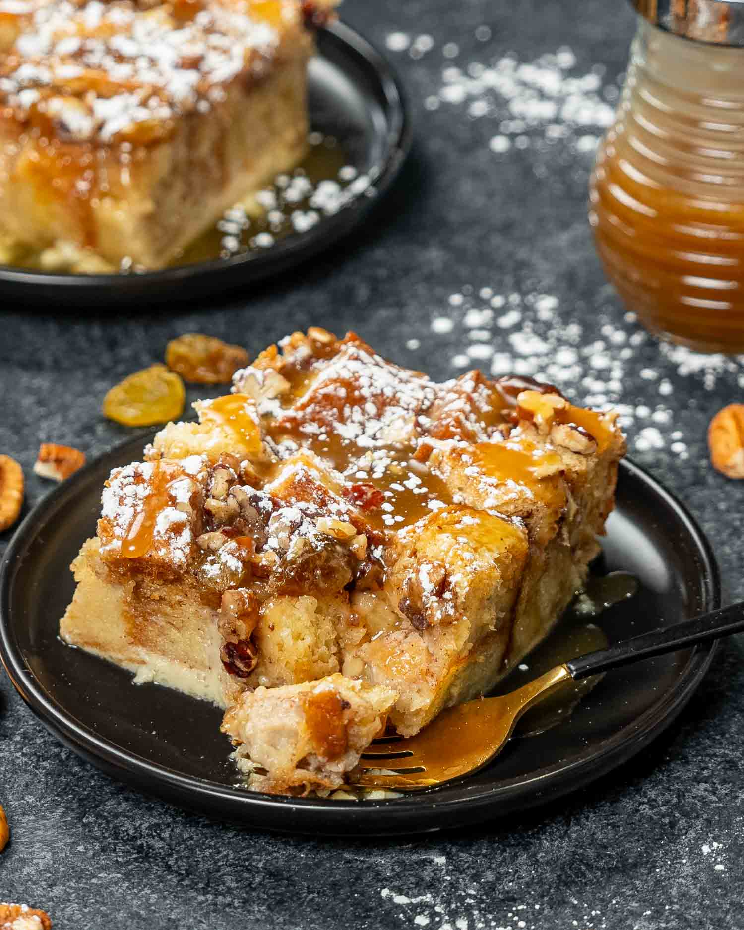 a slice of bread pudding with caramel sauce on a black plate.
