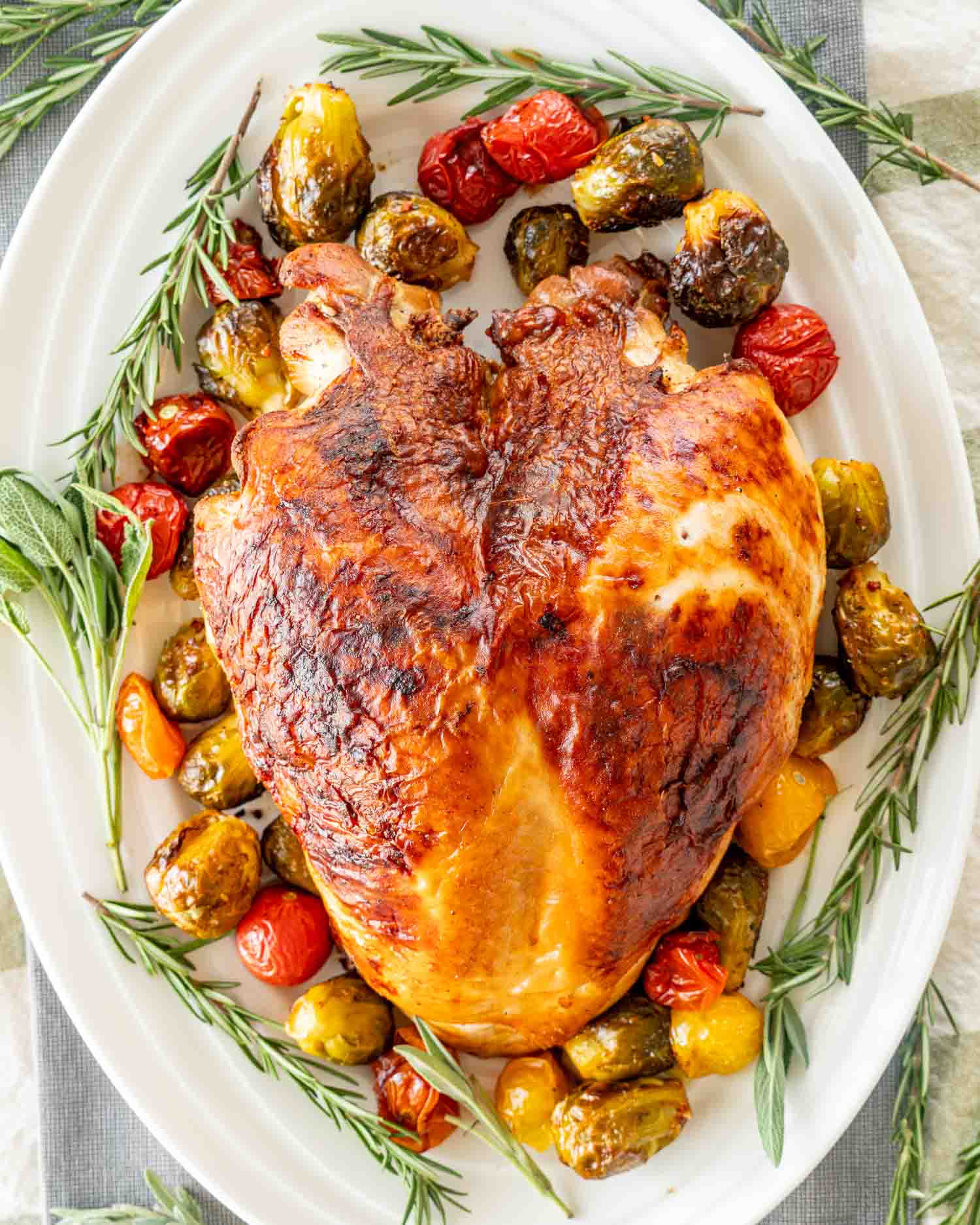a brined roast turkey breast on a turkey platter garnished with veggies and fresh herbs.