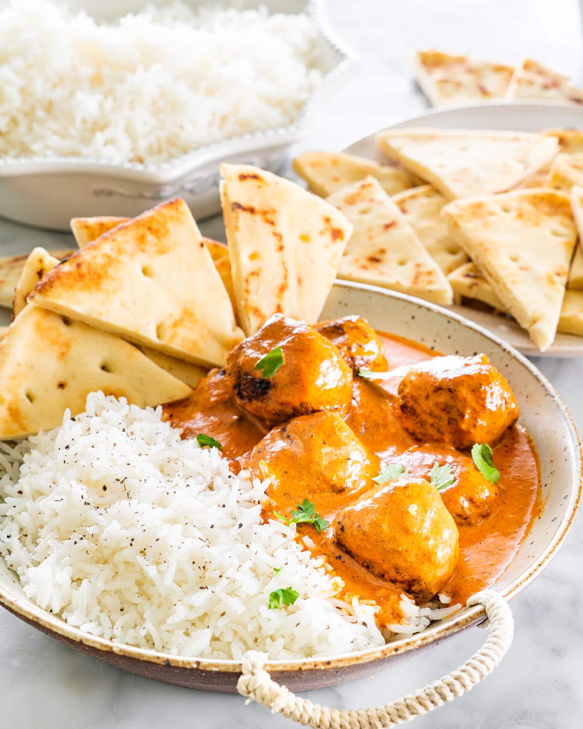 butter chicken meatballs with a side of rice in a bowl with naan slices and garnished with cilantro