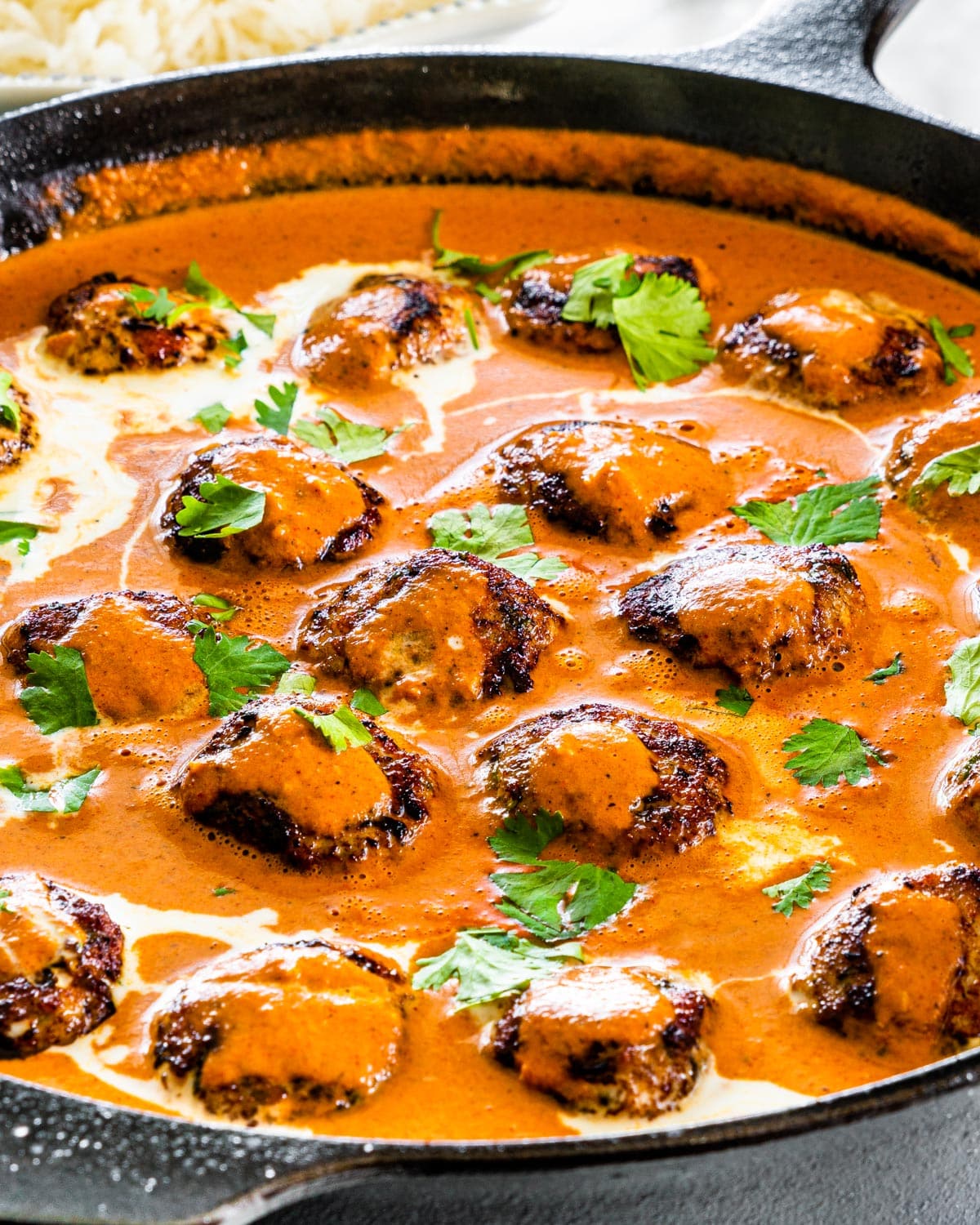 side view shot of freshly made butter chicken meatballs in a black skillet garnished with cilantro