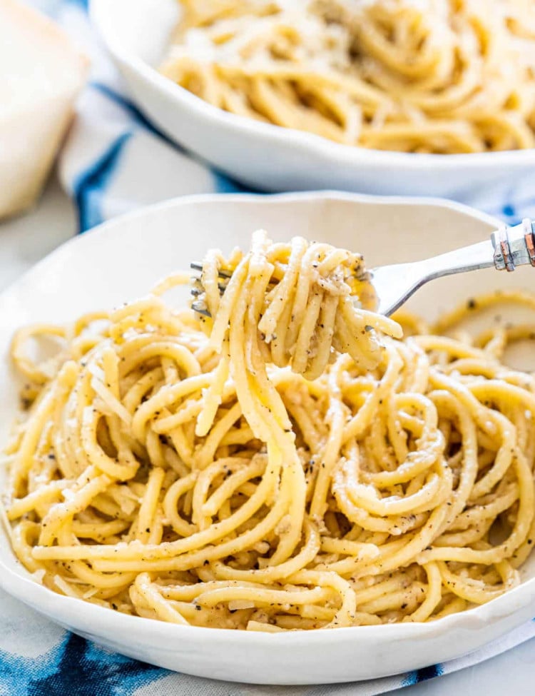 a fork taking a bite of cacio e pepe from a bowl
