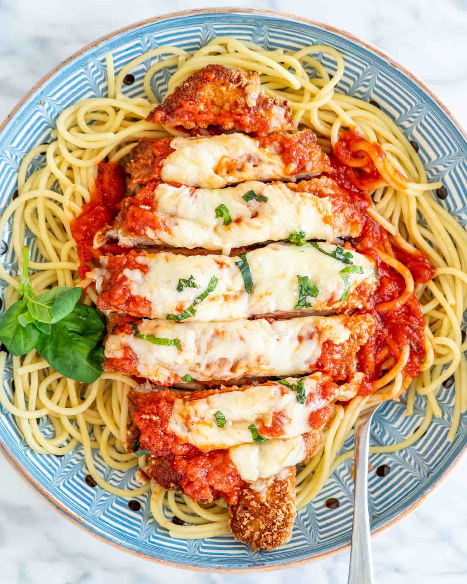 sliced up chicken parmesan on a bed of spaghetti garnished with some fresh basil.