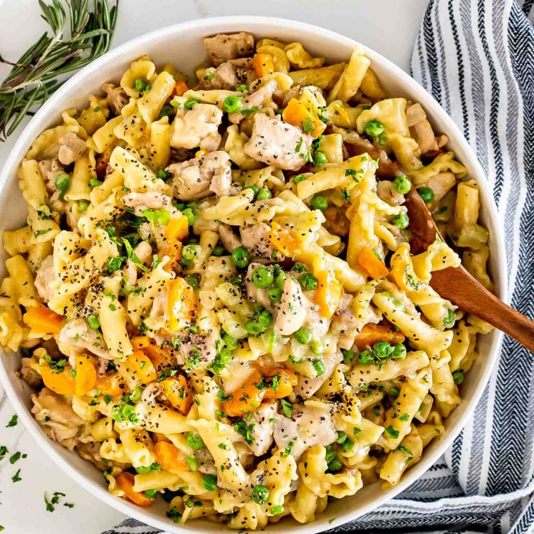 chicken pot pie pasta in a white serving bowl with a wooden serving spoon.
