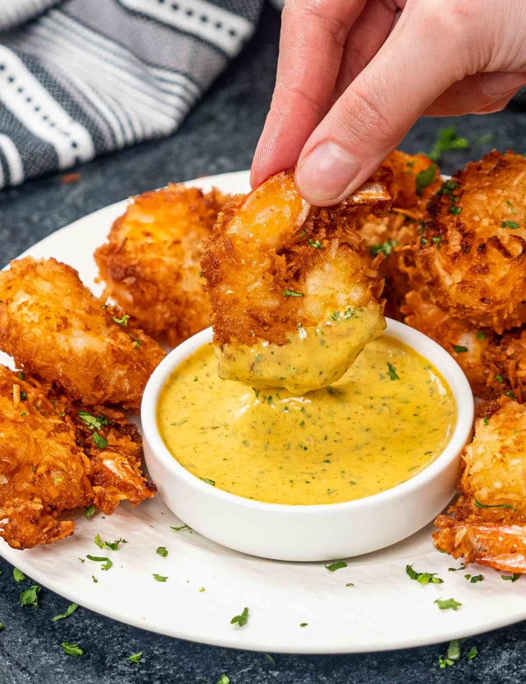a plate full of coconut shrimp with spicy mango dipping sauce in a bowl.