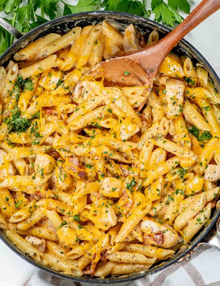 freshly made crack chicken penne with a wooden spoon in a skillet.