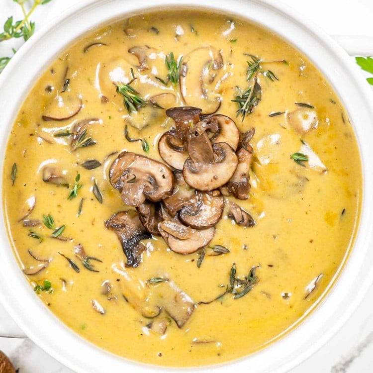 cream of mushroom soup garnished with sauteed mushrooms in a white bowl.