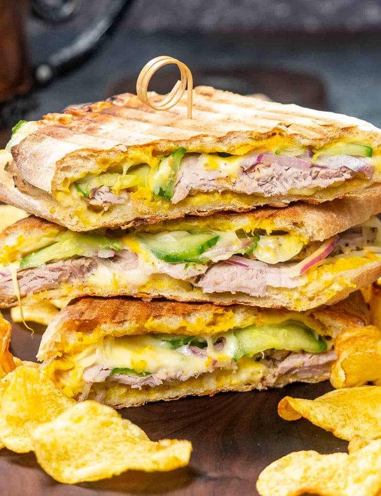 2 cuban paninis sliced in half on a cutting board with potato chips around it.