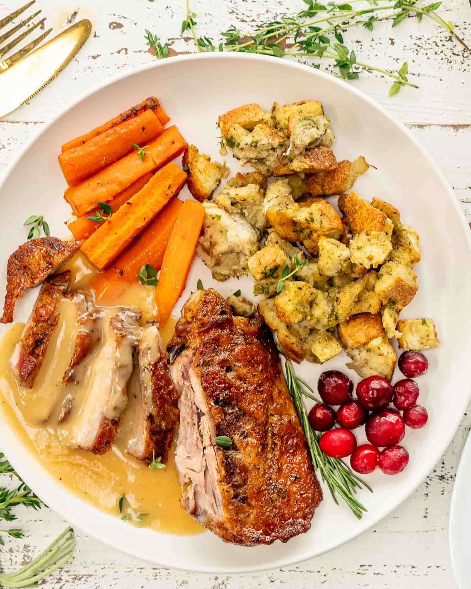 a plate full of stuffing, turkey thigh, carrots and garnished with gravy, cranberries and rosemary.