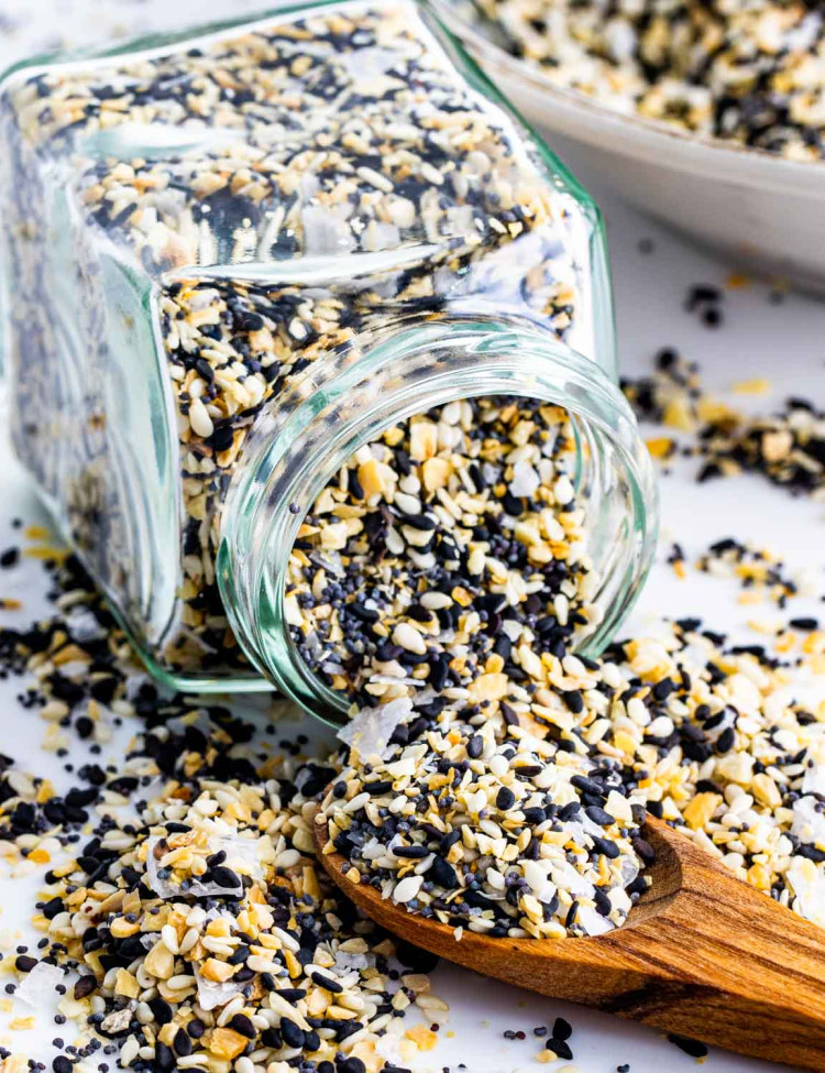 a jar full of everything bagel seasoning on its side with a mini wooden spoon picking some up