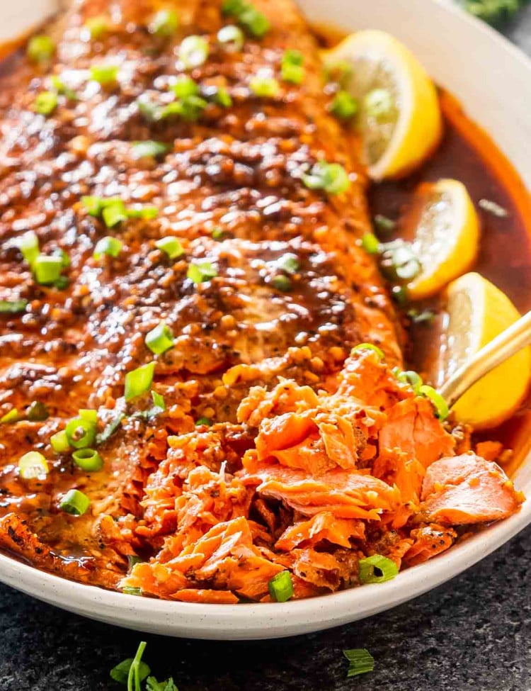 firecracker salmon on a serving platter garnished with lemon wedges and green onions.