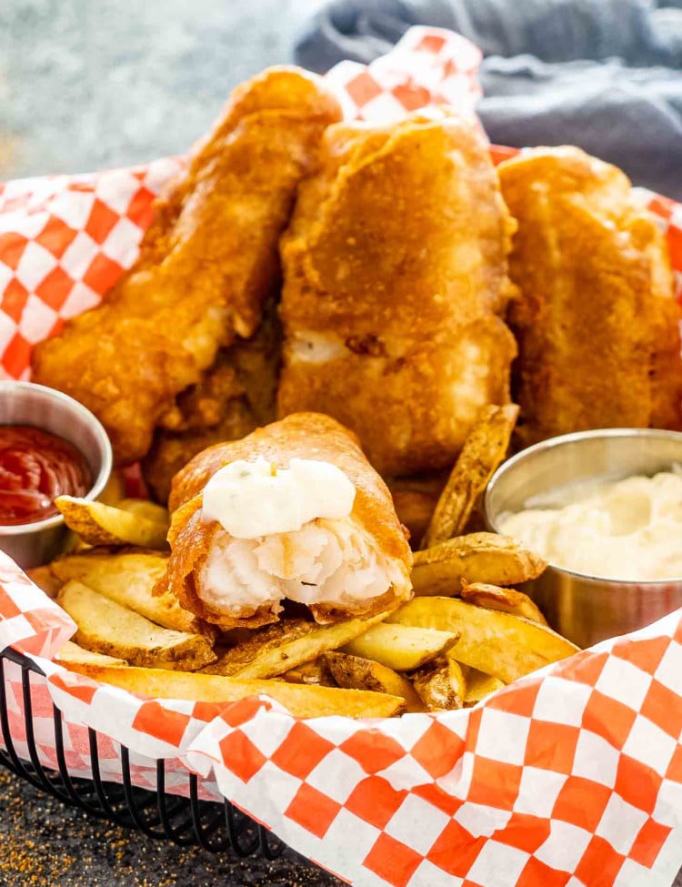 fish and chips in a basket with tartar sauce and ketchup.