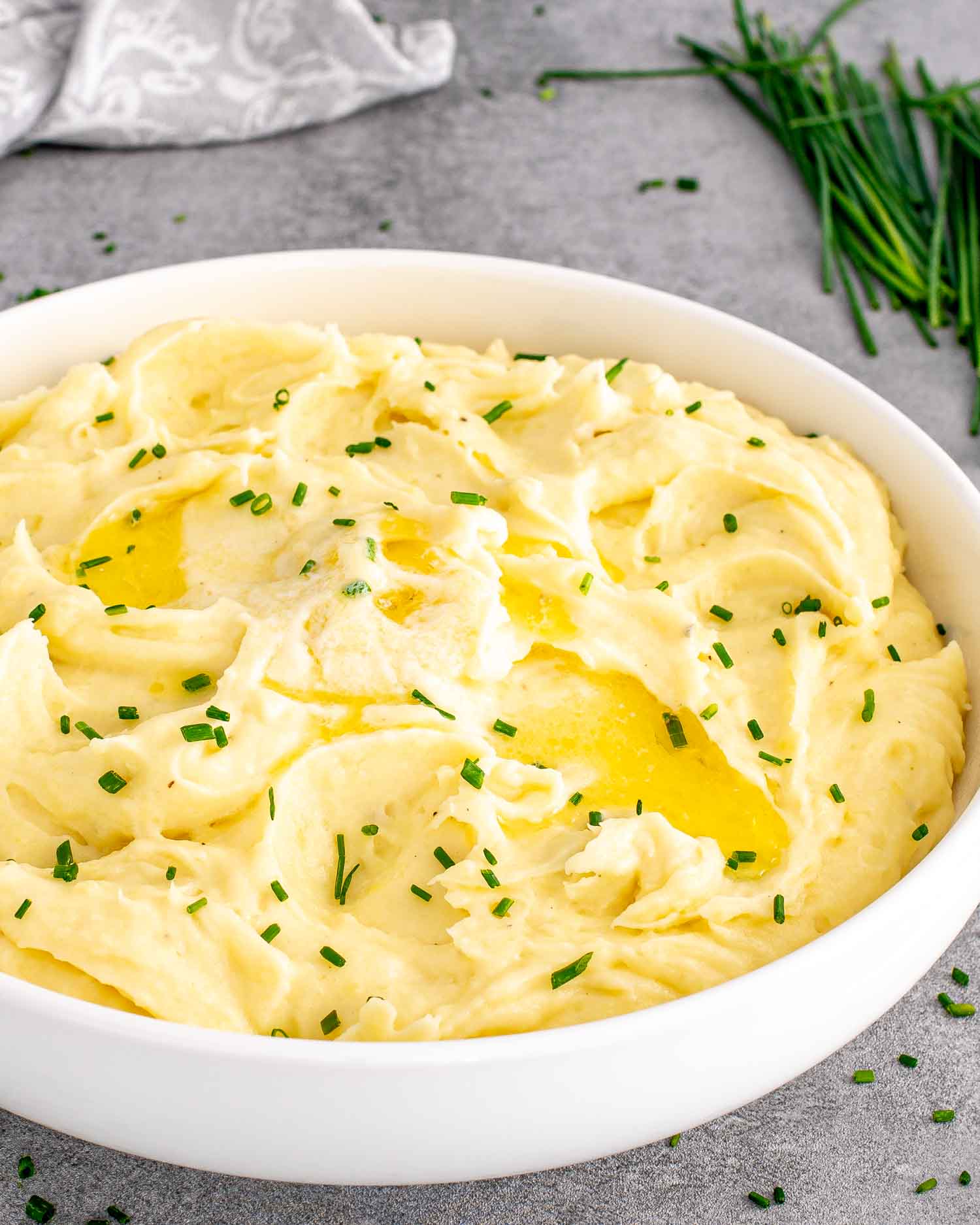 a white bowl with garlic mashed potatoes and a pat of butter on top and garnished with chives.