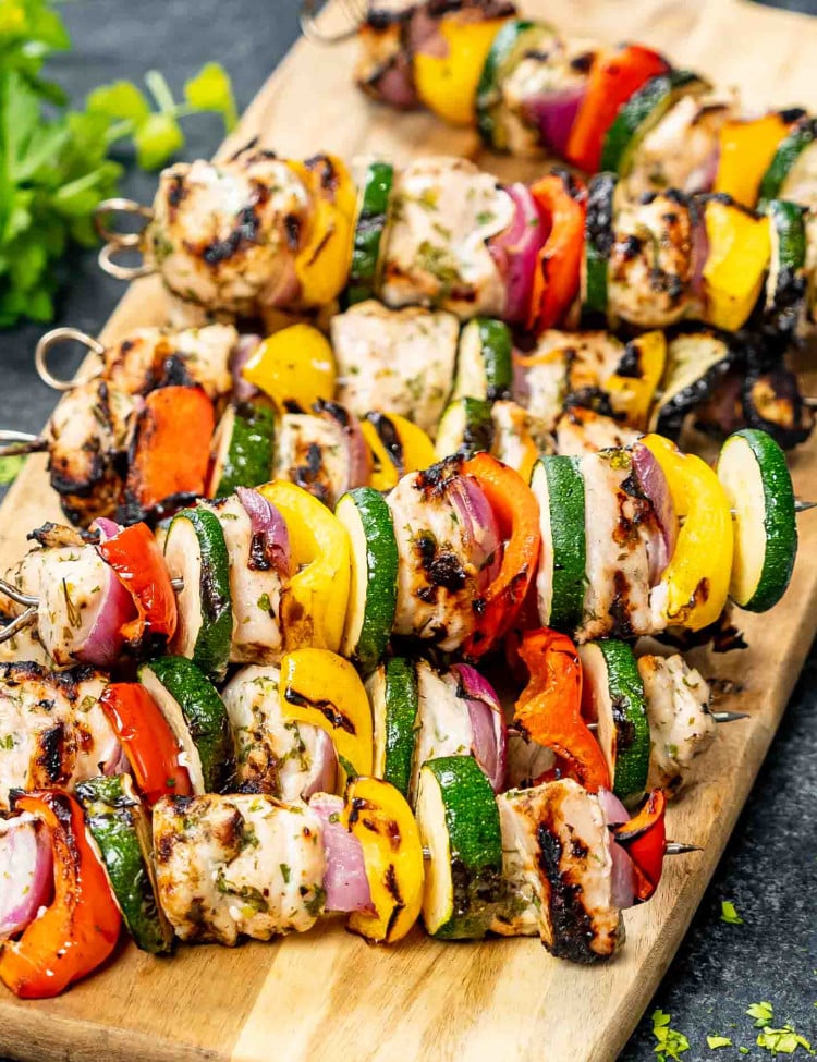 a stack of fresh off the grill grilled chicken kebabs on a cutting board.