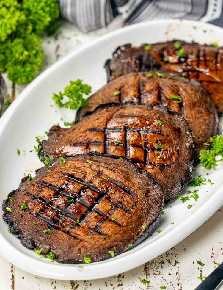 4 grilled portobello mushrooms on a white platter garnished with parsley.