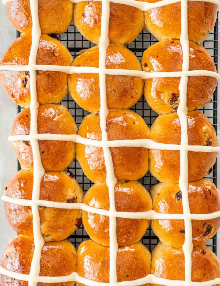 freshly baked hot cross buns on a black cooling rack.