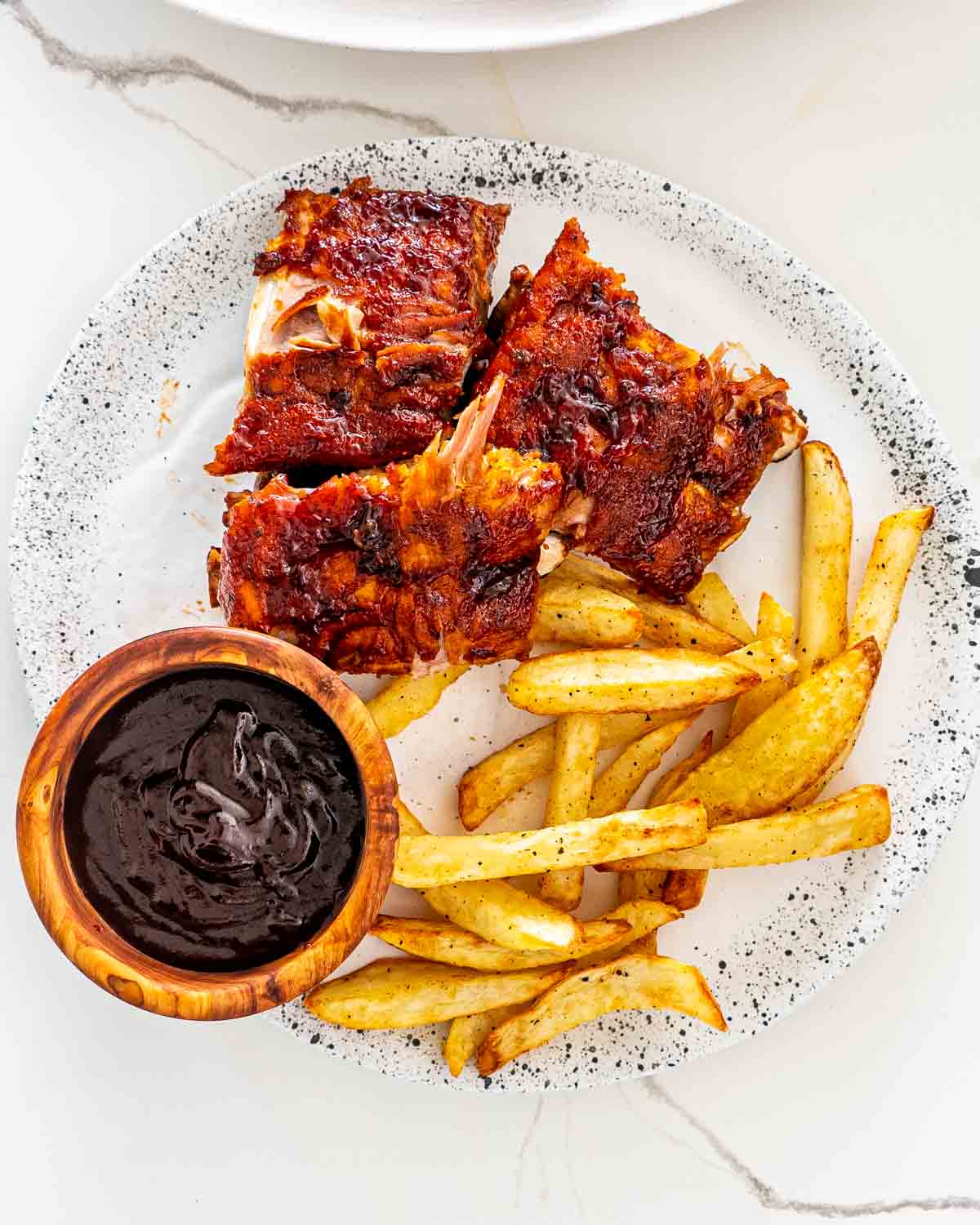 bbq ribs on a plate with french fries and bbq sauce.