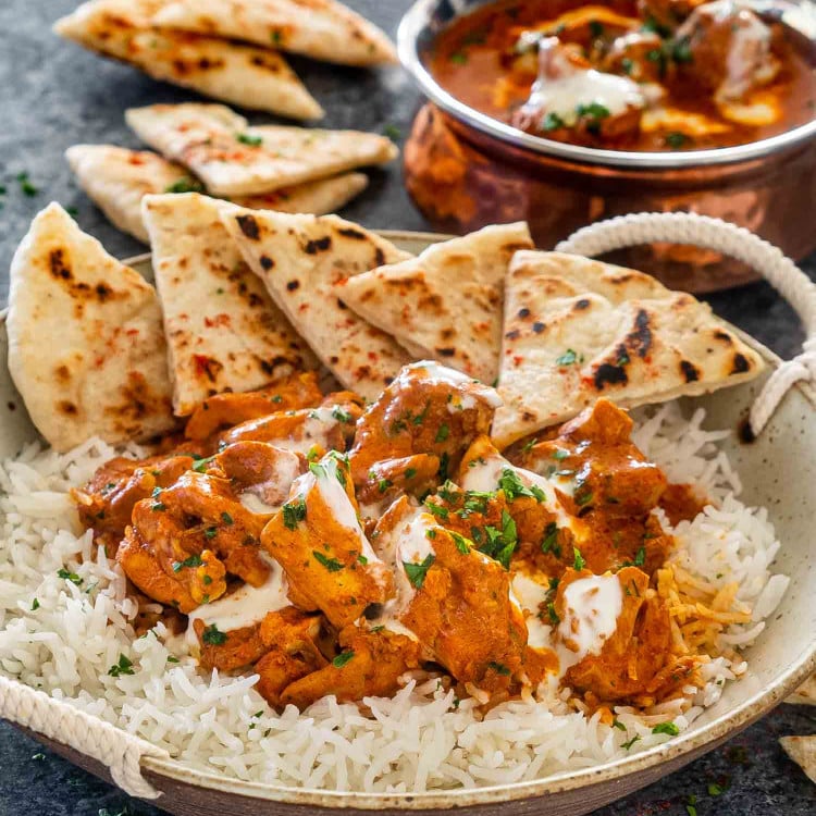 butter chicken over a bed of rice on a plate with naan.