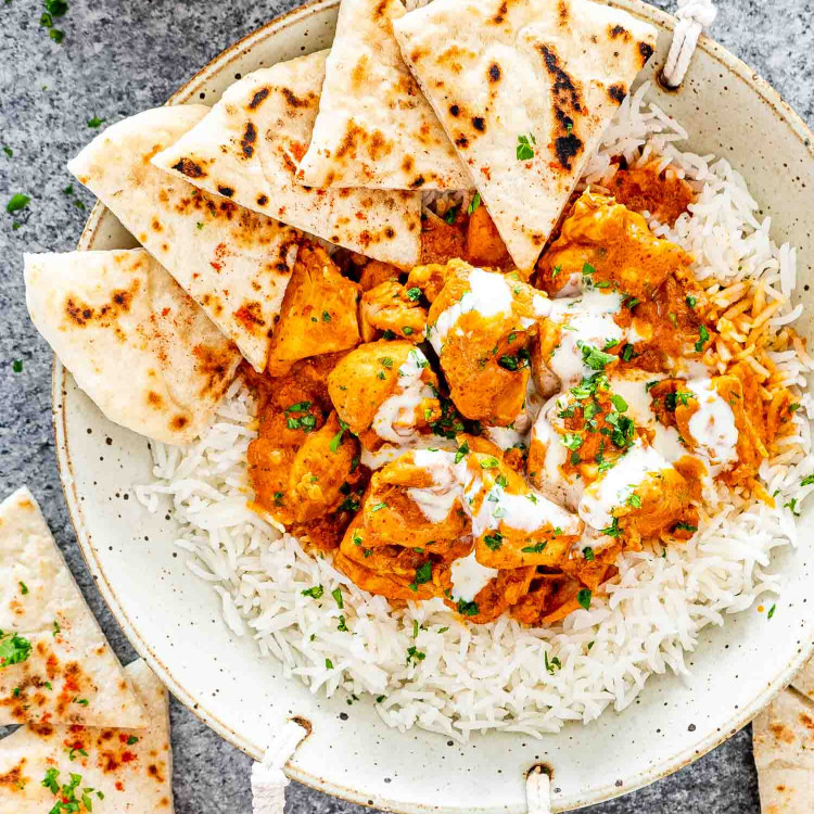 butter chicken over a bed of rice on a plate with naan.