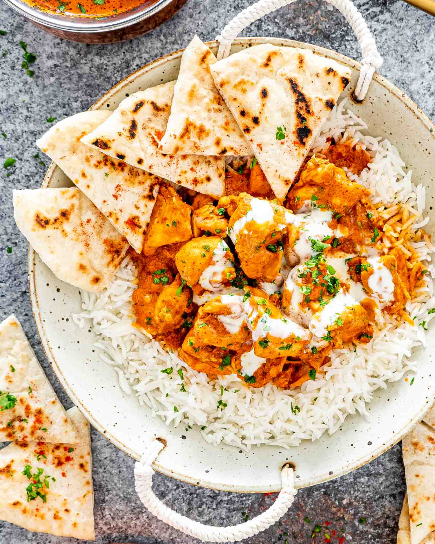 butter chicken over a bed of rice on a plate with naan.
