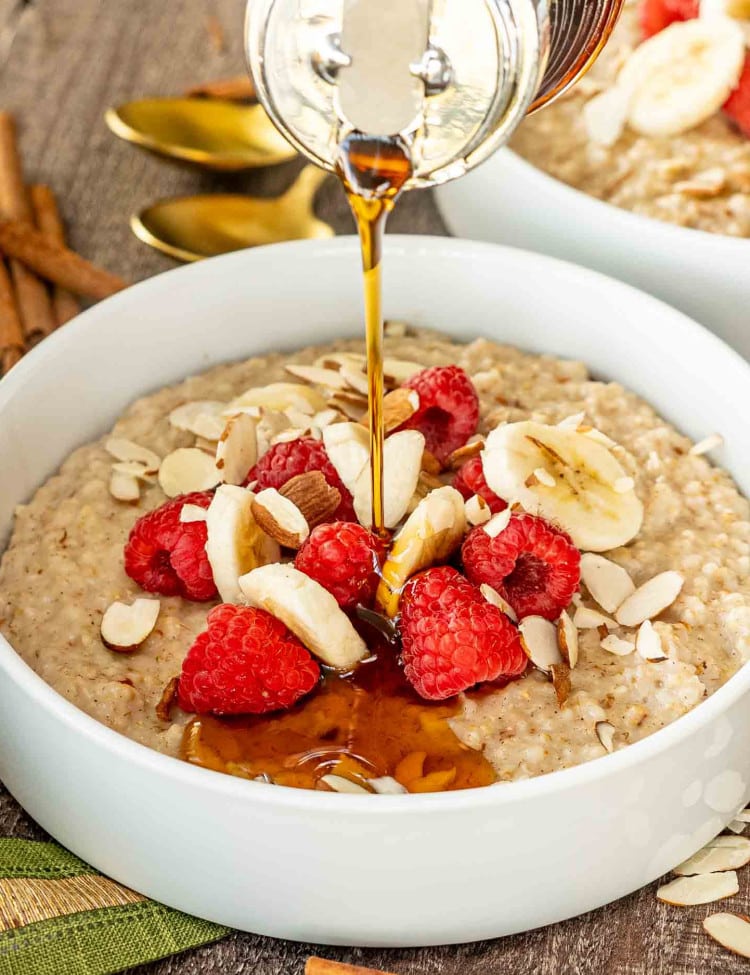 a big white bowl loaded with instant pot steel cut oats garnished with bananas, raspberries, and some sliced almonds.