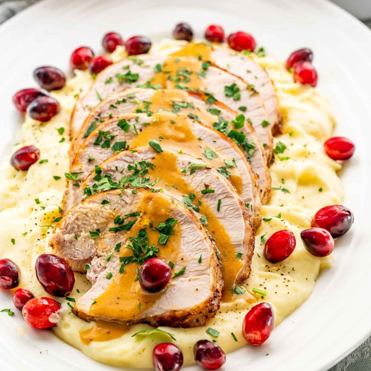 instant pot turkey breast cut in slices over a bed of mashed potatoes garnished with gravy, parsley and cranberries.