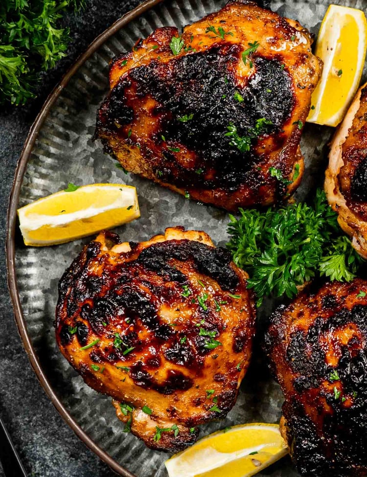 jerk chicken thighs on a platter garnished with lemon wedges and parsley.