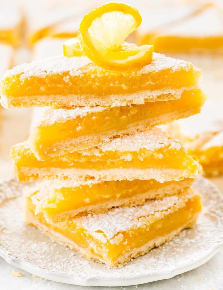 lemon bars cut into triangles stacked on top of each other on a white plate.
