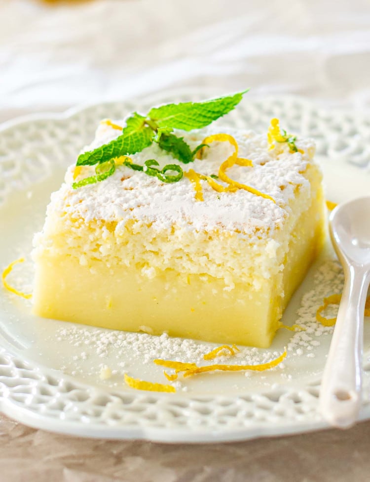 a slice of lemon magic cake garnished with mint on a white plate.