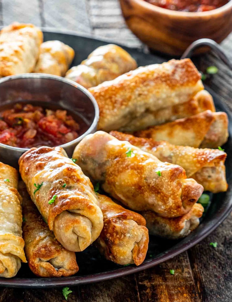 egg rolls on a metal platter with a bowl with salsa in the middle.