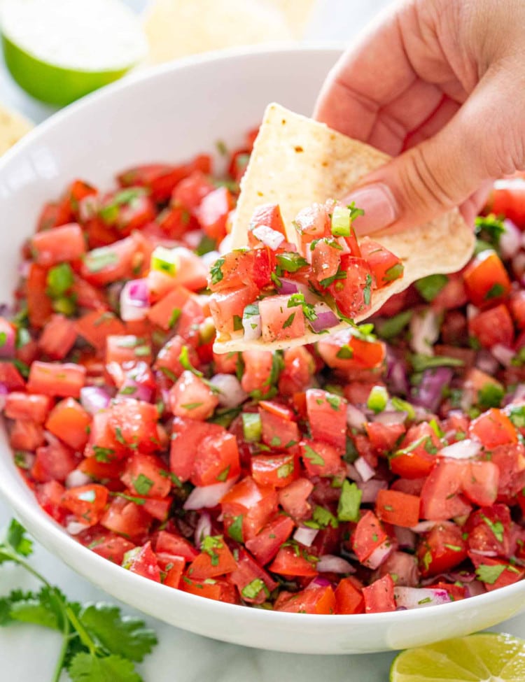 a hand lifting some pico de gallo with a tortilla chip.