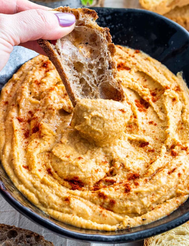 red lentil hummus in a big black bowl garnished with a bit of smoked paprika.
