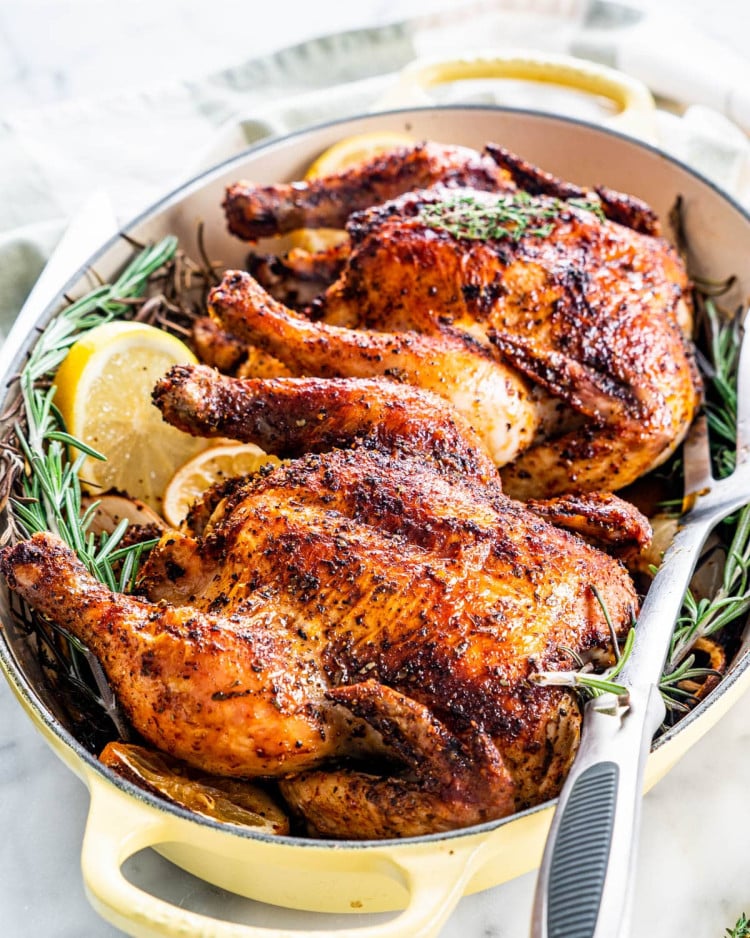 two roasted cornish hens in a roasting pan with sprigs of rosemary and lemon slices
