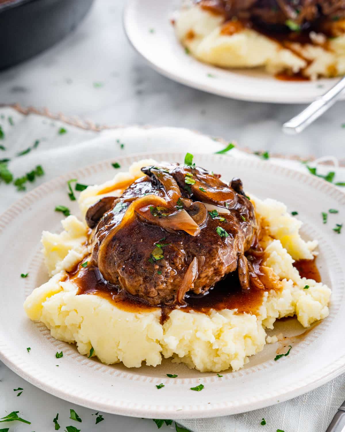 a salisbury steak with mushroom gravy over a bed of mashed potatoes on a white plate