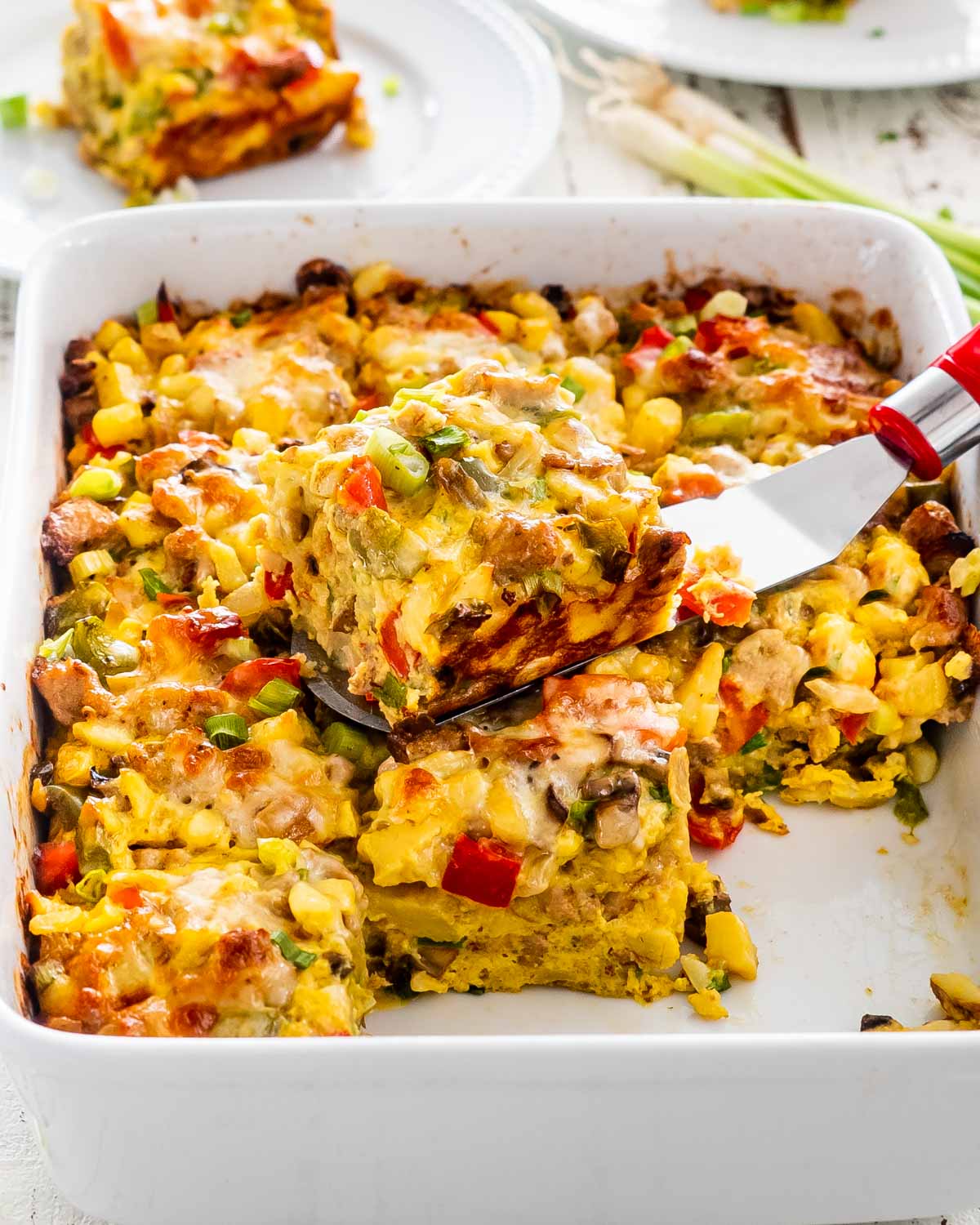 sausage potato breakfast casserole cut into slice with a spatula with a slice on top of the casserole.