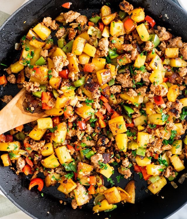 overhead shot of sausage and potato hash being stirred by a wooden spoon