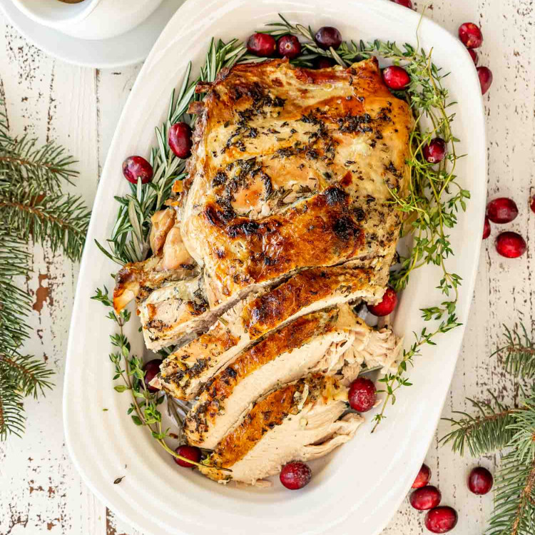 Whole slow cooked turkey breast on festive platter with cranberries and herbs, ready for serving.
