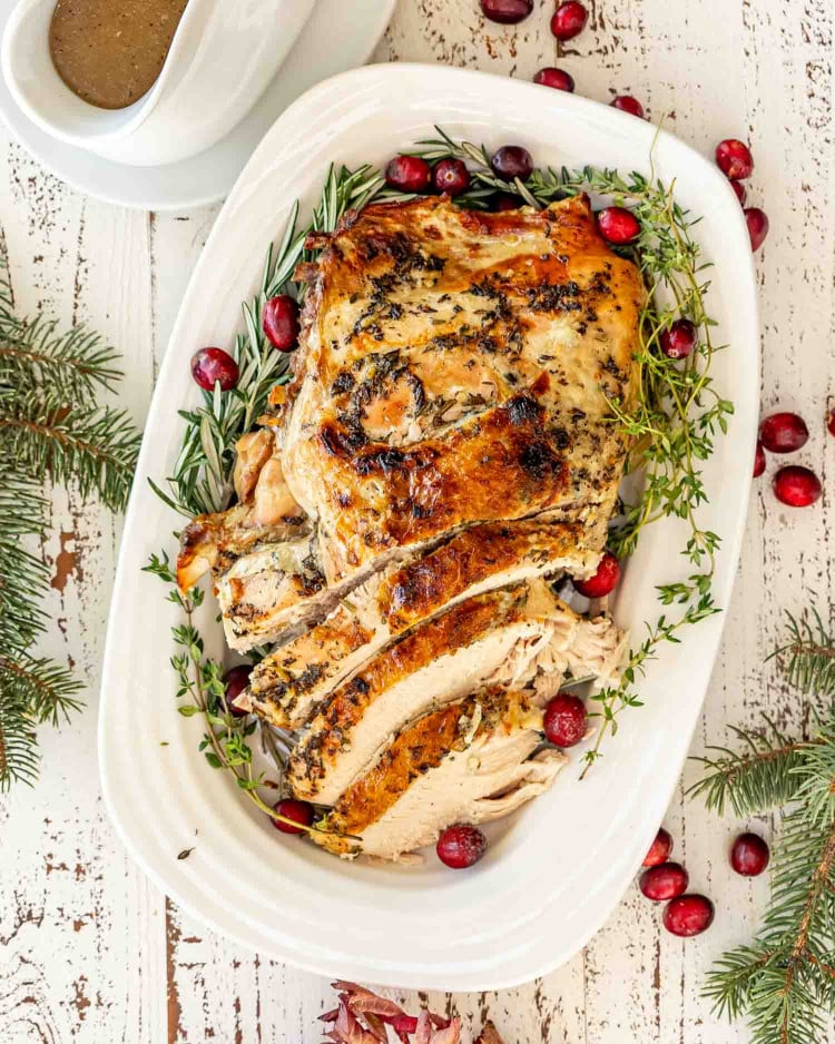 Whole slow cooked turkey breast on festive platter with cranberries and herbs, ready for serving.