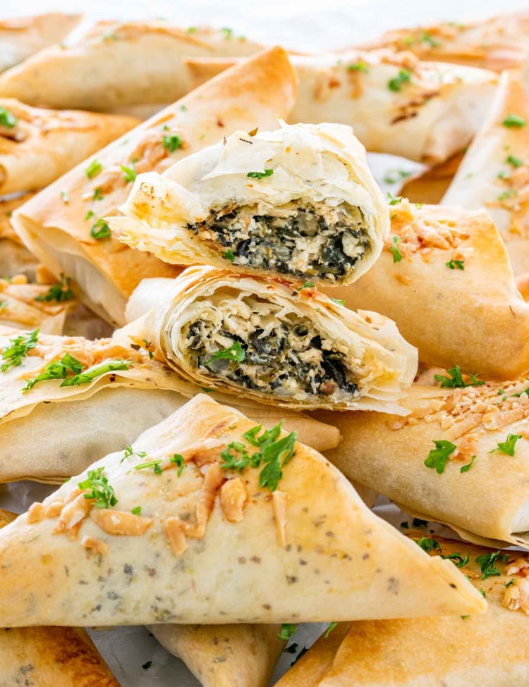 a bunch of spanakopita triangles on a white platter.