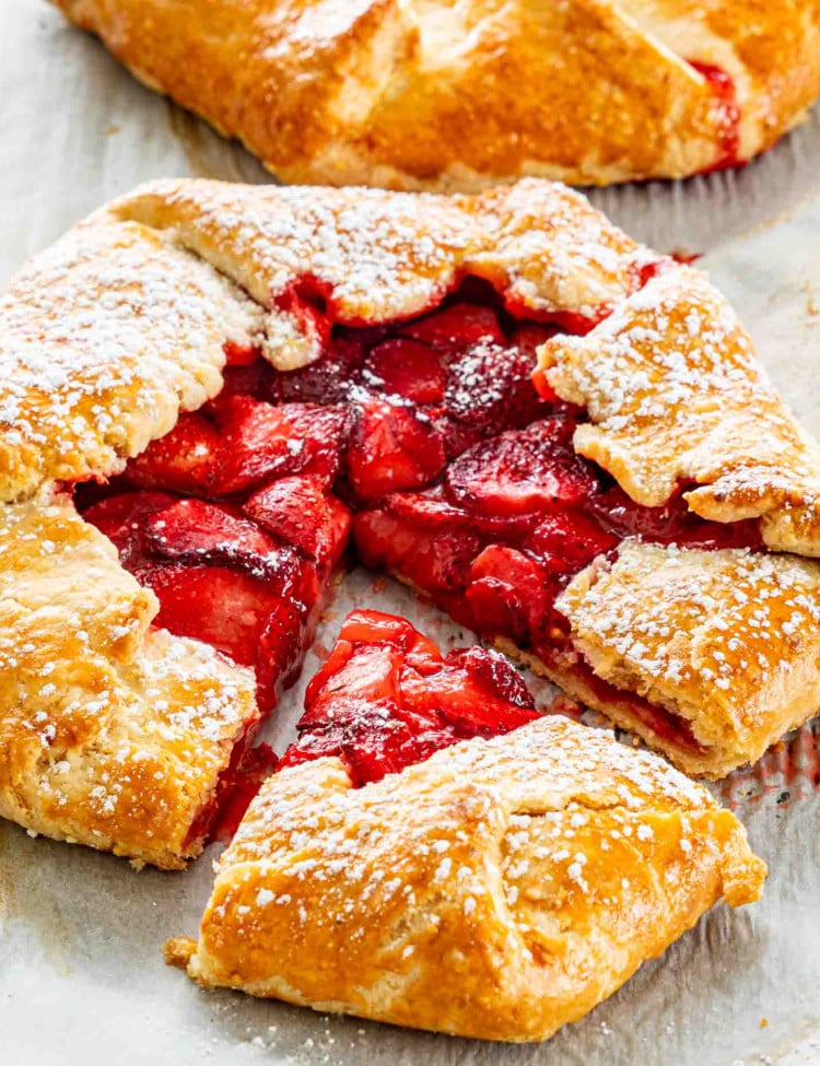 side view shot of a strawberry galette on parchment paper sprinkled with some powdered sugar and a piece cut out of it.