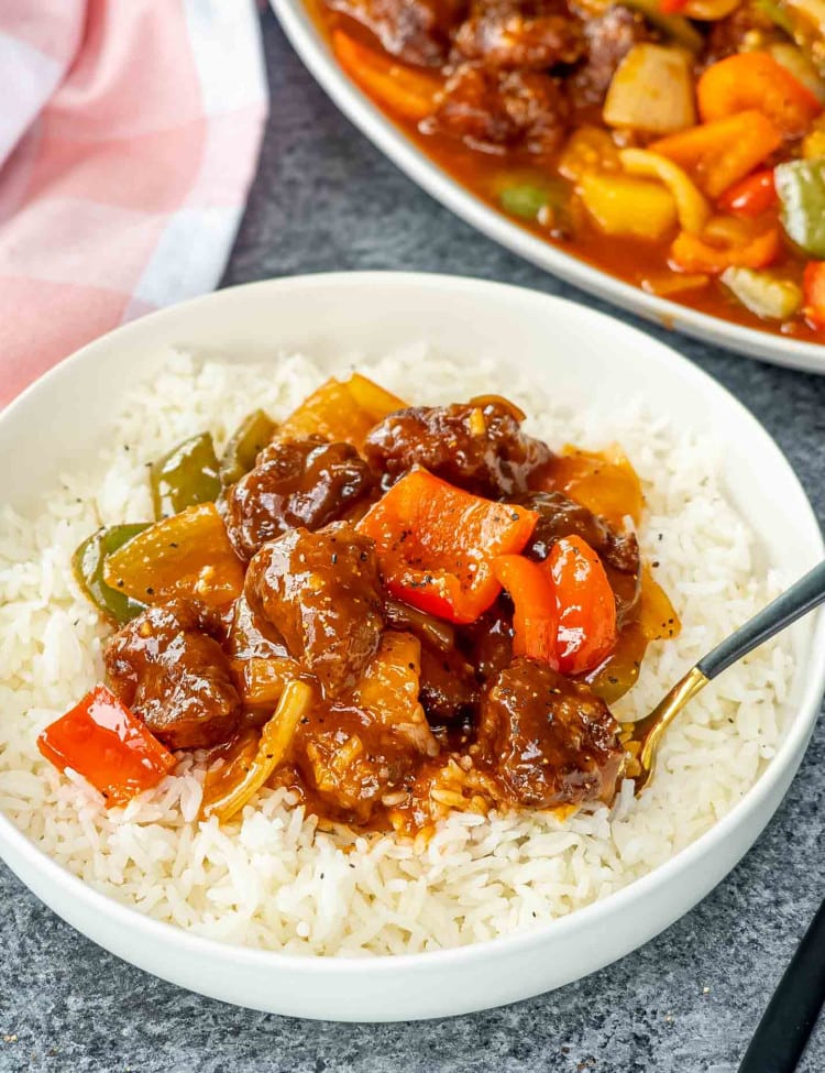 sweet and sour pork on a bed of rice in a white bowl.