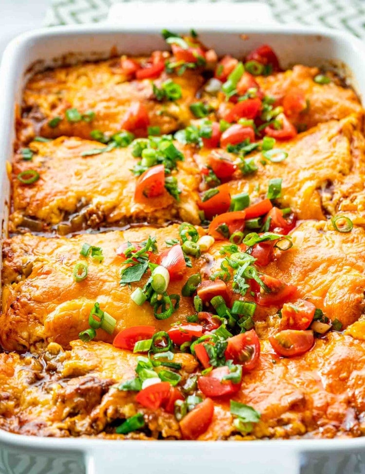 freshly made taco lasagna in a white casserole dish garnished with tomatoes and avocado.