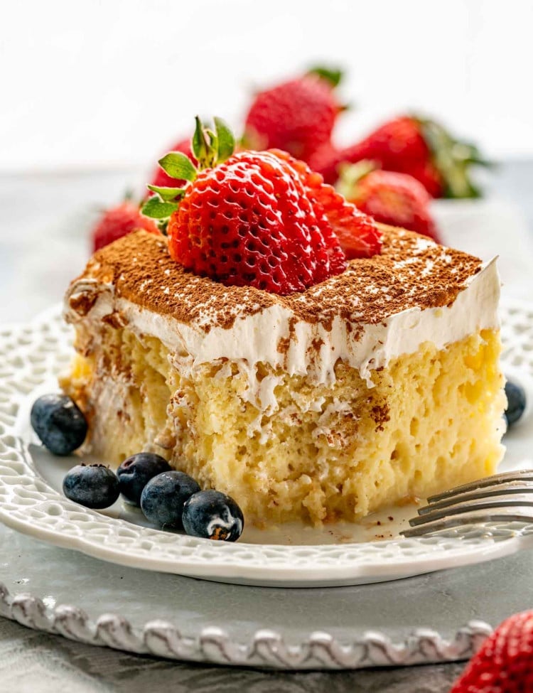 a slice of tres leches cake with a sliced strawberry on top on a white plate.