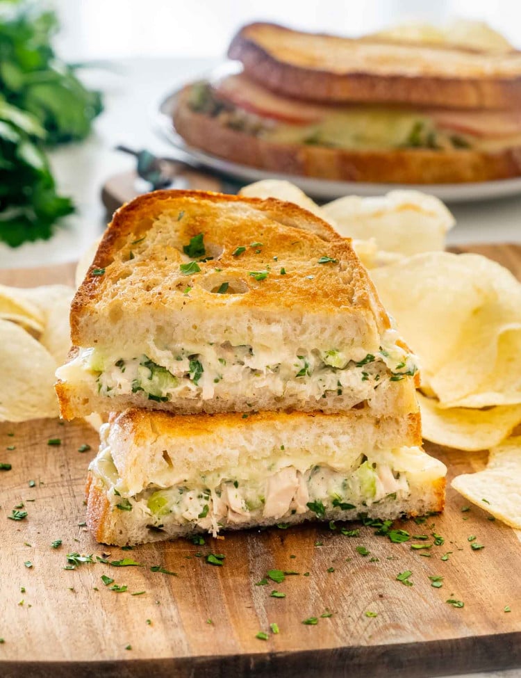 a tuna melt sandwich cut in two on a cutting board with potato chips.