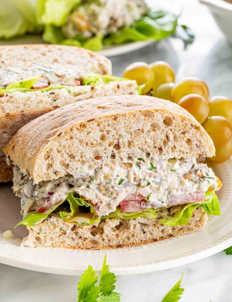 side view shot of a tuna salad sandwich on a plate with grapes.